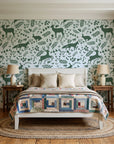 Woodland Hush Sage woodland animal wallpaper behind a white cottage bed with a patchwork quilt in a cozy cottagecore bedroom
