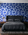 Woven Whisper Cobalt abstract heart wallpaper behind a tufted headboard in a dark, moody bedroom
