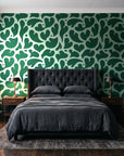 Woven Whisper Emerald abstract heart wallpaper behind a tufted headboard in a dark, moody bedroom